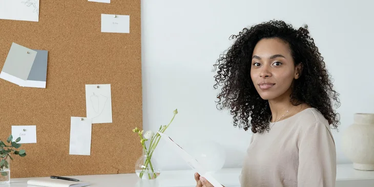 A woman sitting near a bulletin board.