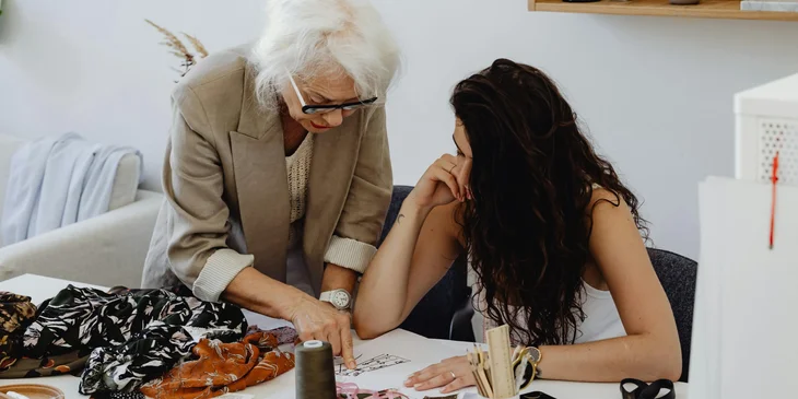 A designer teaches the basics of fashion design to her apprentice.