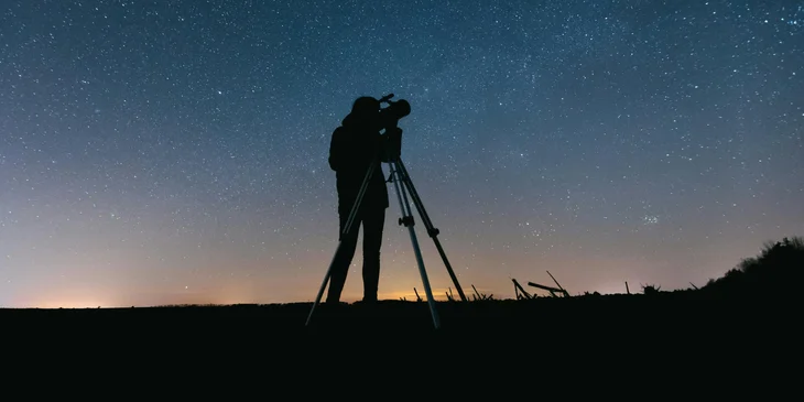 An astronomer looking through a telescope at night.