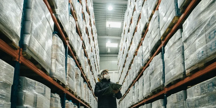 An automated logistics specialist holding a clipboard in a warehouse and conducting an inventory of stocks.