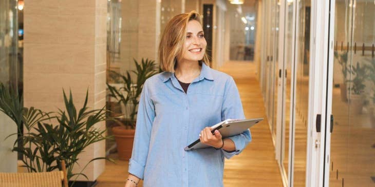 Una donna con un tablet in mano che cammina in un ufficio.