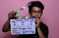 Un ragazzo che tiene in mano un ciak su uno sfondo rosa.