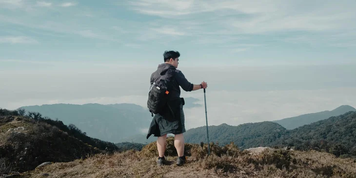 A backpacker standing on a rock looking at a mountain scenery.