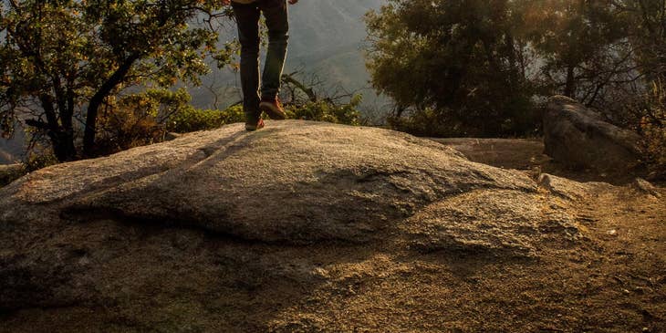 Backpacker standing on a rock looking at mountain scenery.