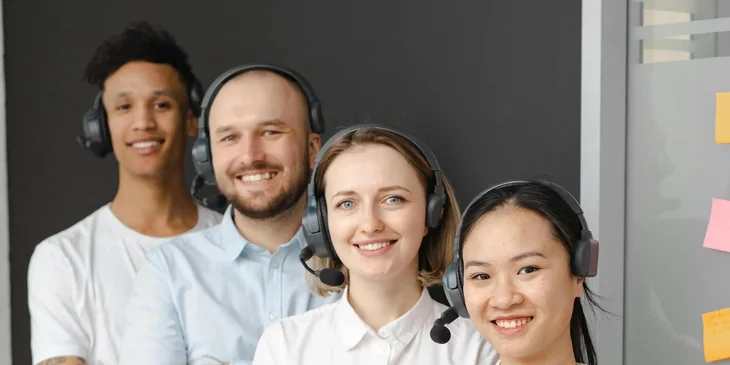 Vier Mitarbeiter eines Callcenters stehen lächelnd nebeneinander.