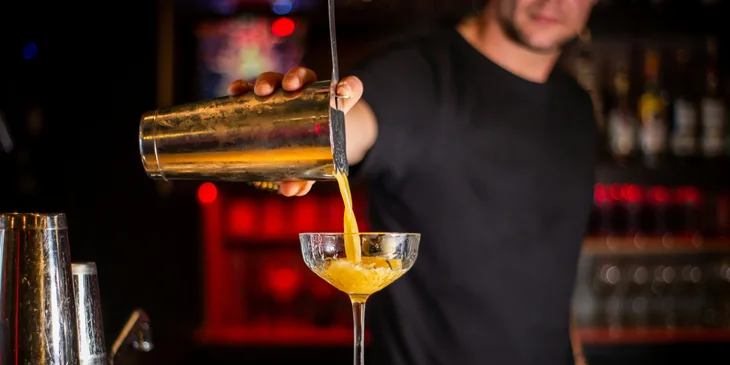 A bartender pouring an alcoholic beverage into a glass.