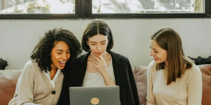 Three women sitting on a sofa in front of a laptop.