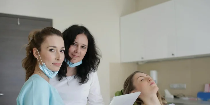 A dentist and a dental assistant stand beside a patient.