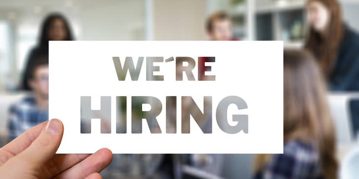 Hand holding up a sign that says, "We're hiring."