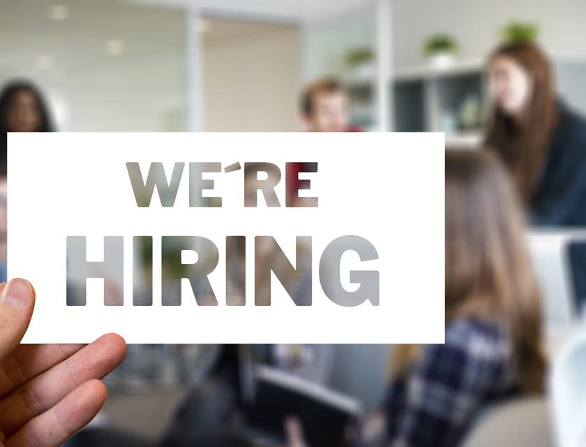 Hand holding up a sign that says, "We're hiring."