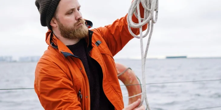 A man in an orange jacket holding a rope.