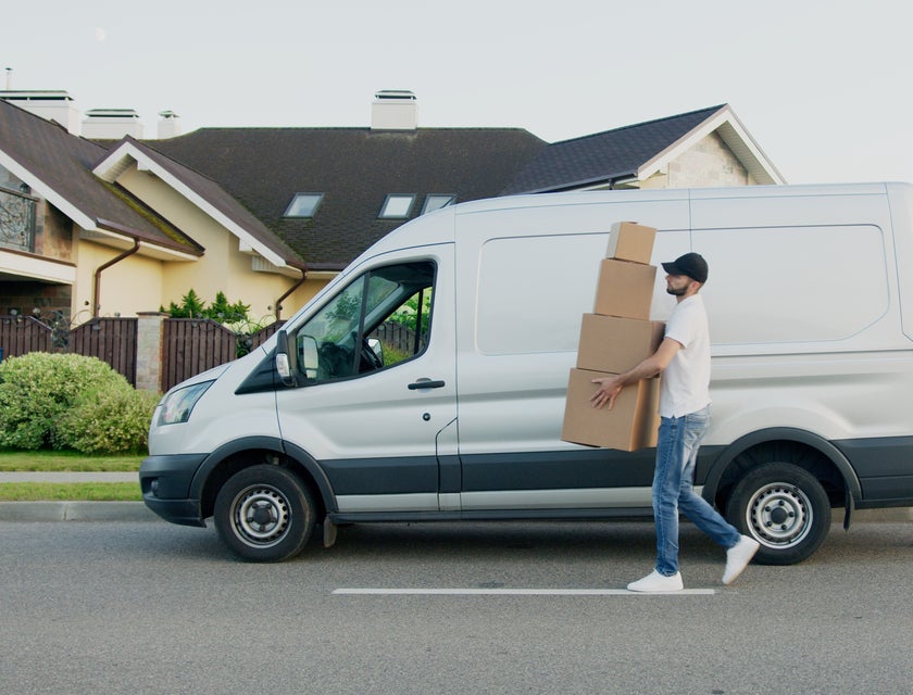 Un repartidor llevando paquetes a un punto de entrega designado, desde su camión de mensajería.