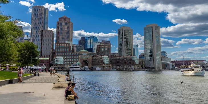 A view of the Boston Harbor cityscape beneath clear blue skies.