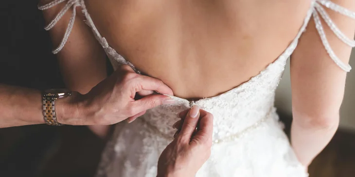 A bridal stylist fitting a dress on the bride.