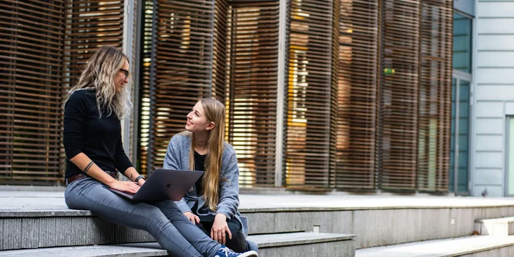 Two women having a conversation by the stairs outside.