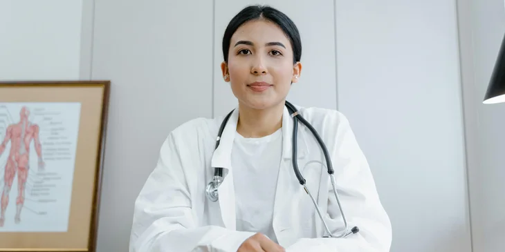 A physician in a white scrub suit wearing a black stethoscope.