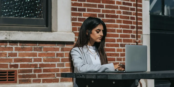 A female typing on a laptop in town.