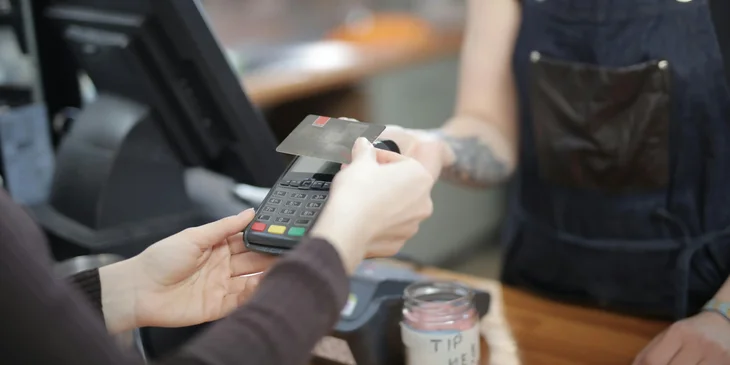 A client paying with a card through a POS terminal handed over by the cashier.