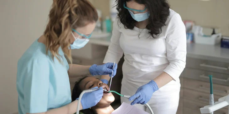 A certified medical assistant is assisting the dentist in performing a dental procedure.