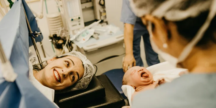 A certified nurse midwife carrying the newborn and showing to the mother.