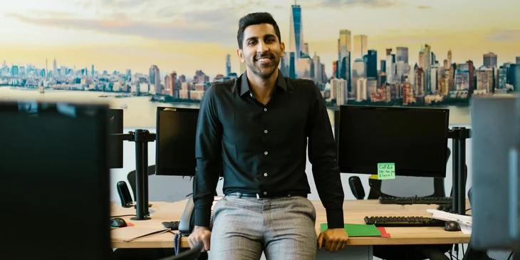 A man in black shirt sitting on a desk.