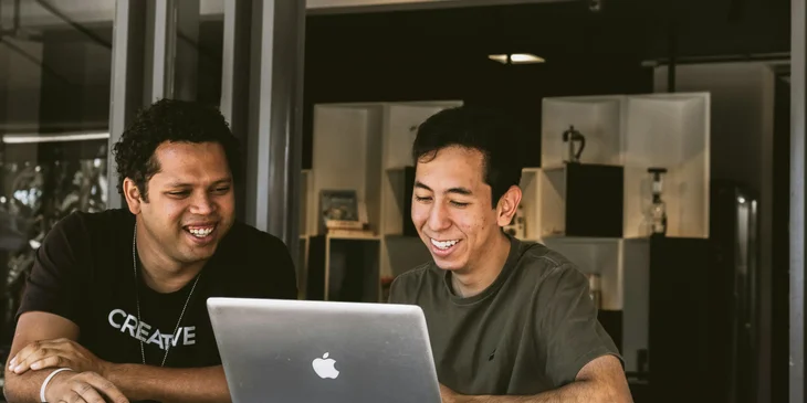 Two smiling colleagues happily working on a report in the office.