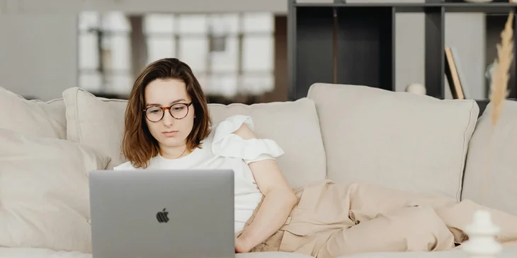 A woman lying on a couch while working at home.