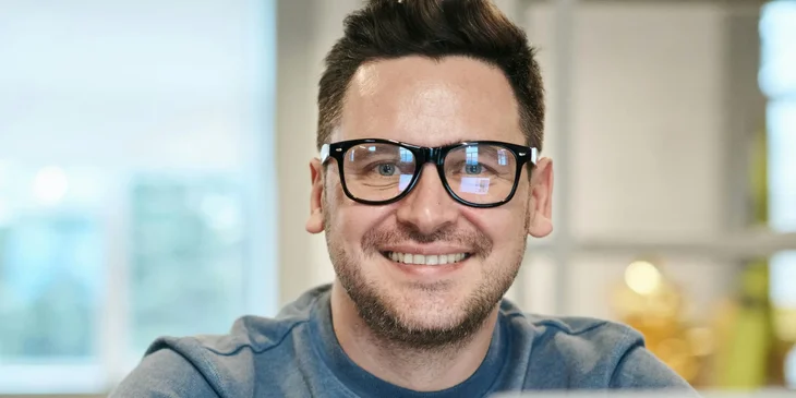 A man wearing glasses smiling while looking at the camera.