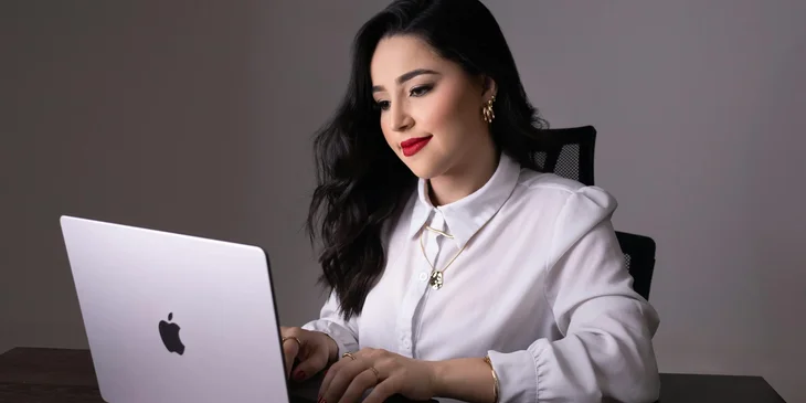 A woman in an office smiling while typing on a laptop.