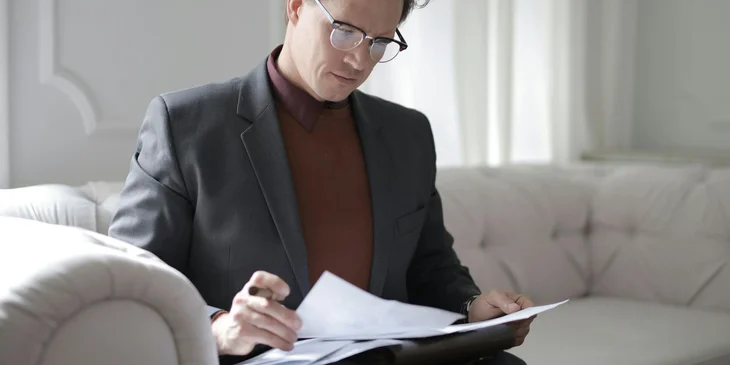 A compliance auditor sitting on a white couch, reviewing and analyzing company records.
