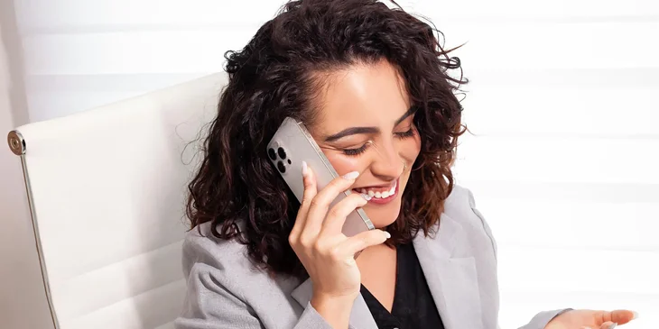 Ejecutiva en su oficina sonriendo y hablando por teléfono celular.
