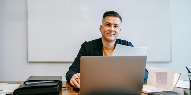 A man smiling while sitting at his desk.