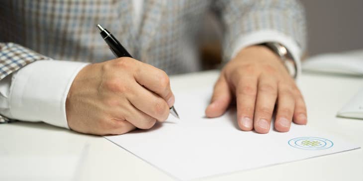 A man in a gray suit signing a contract with a black pen.