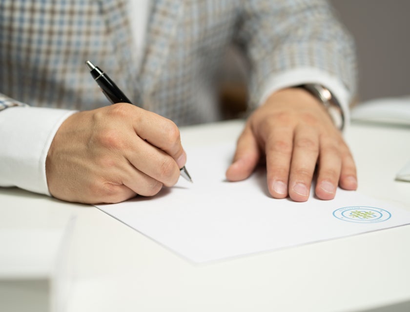 A man in a grey suit signing a contract with a black pen.