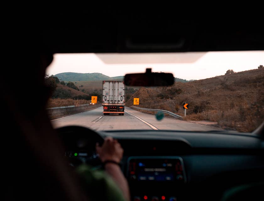 Conductor de camión sosteniendo el volante de su trailer con la vista trasera de un transporte de carga frente a él.
