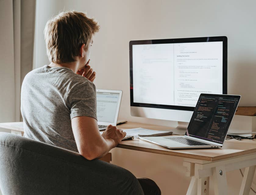 Una desarrollador PHP trabajando en un programa de codificación con tres computadoras.
