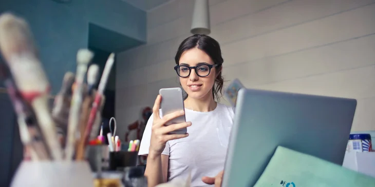 A woman using her phone while at her workdesk.