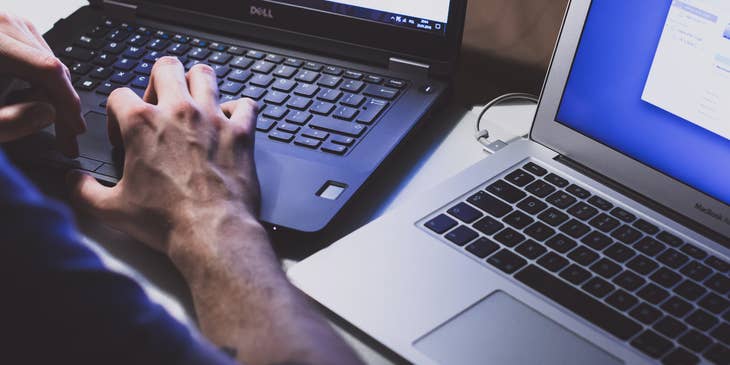 A person using two laptops to improve a company's cybersecurity.