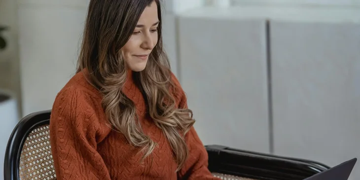 A woman in a red sweater working on her laptop.