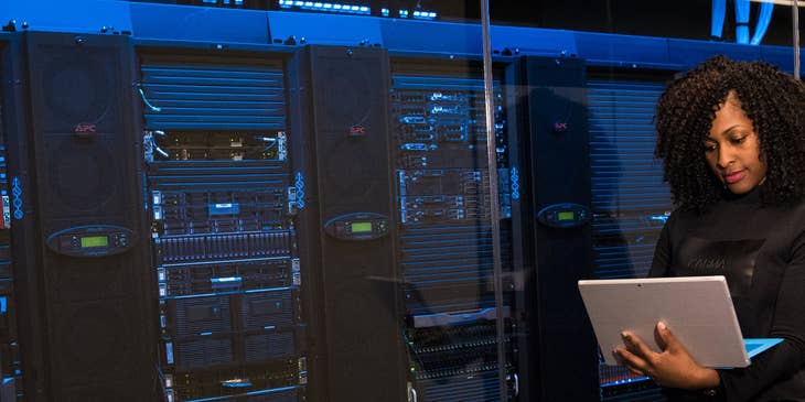 Data scientist working on a laptop next to server racks.