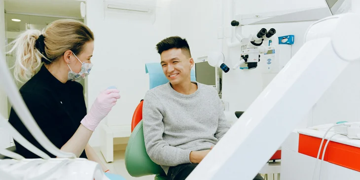 A dentist talking to a patient sitting in a dental chair.