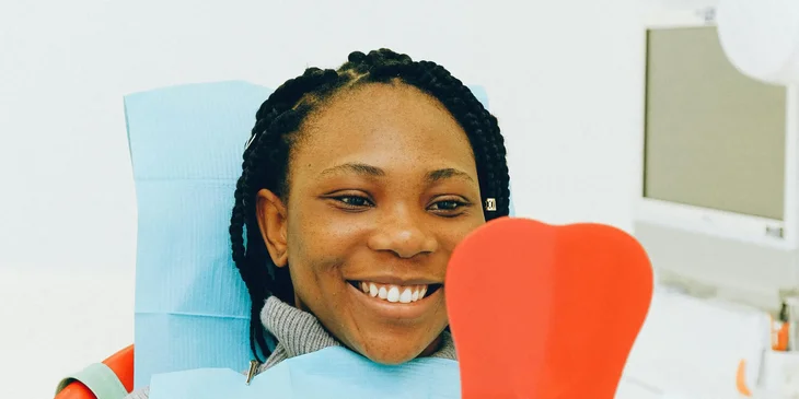 A woman in a dental chair smiling and looking at the mirror.