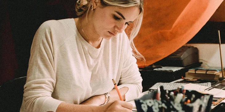 A woman in white long sleeve shirt drawing on a white paper.