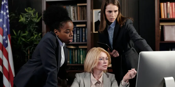 A female district attorney investigator working with district attorneys and reviewing documents on the computer.