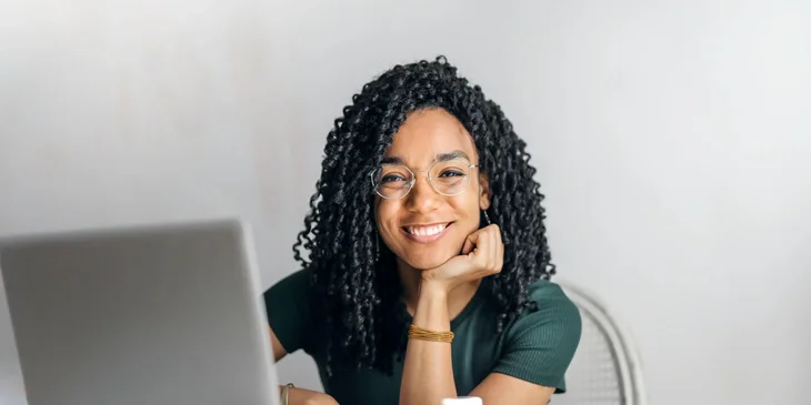 A smiling woman sitting at a table with a laptop in front of her.