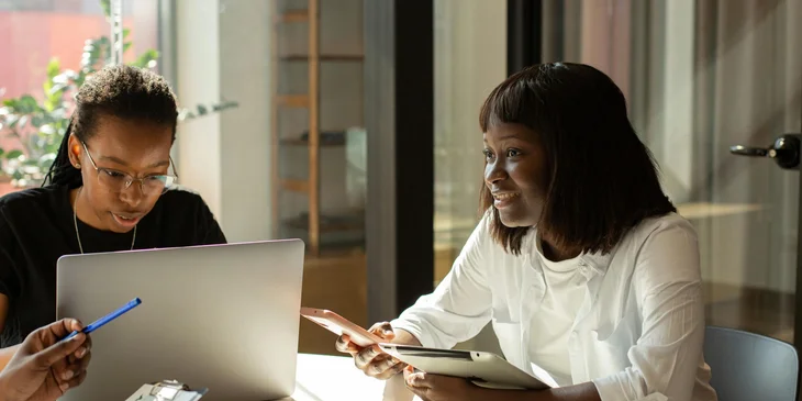 Two women sitting next to each other inside an office.