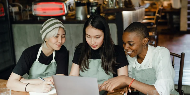 Three female coworkers using a laptop to upload content to the shop's social media page.