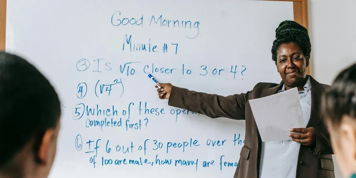 A teacher pointing at the board while explaining the lesson.