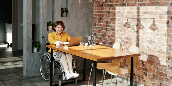 A woman in a wheelchair happily working on her laptop.