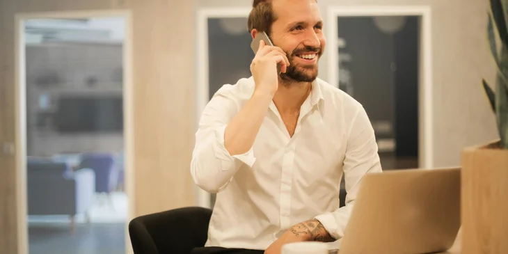 A man talking on the phone while using a laptop.
